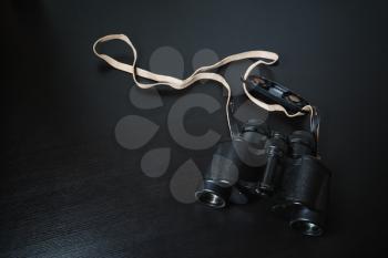 Photo of old black binoculars on black wood table background.