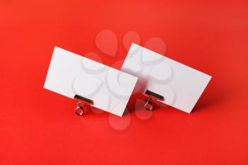 Two blank business cards and metal binder clips on red paper background.