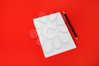 Blank copybook and pencil on red paper background. Blank branding template. Blank stationery. Mockup for branding identity for placing your design.