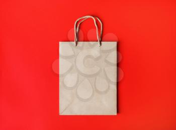 Blank brown paper bag with rope handles on red paper background. Top view. Flat lay.
