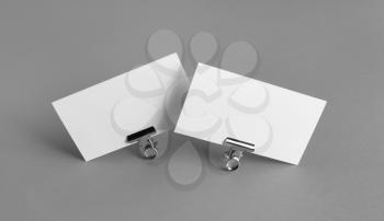 Two blank business cards and metal binder clips on gray background.