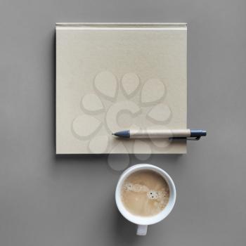 Blank kraft book, pen and coffee cup on gray paper background. Template for branding design. Top view. Flat lay.