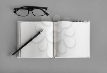Photo of blank book, pencil and glasses on gray background. Responsive design mockup. Stationery elements. Top view. Flat lay.