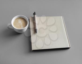 Closed booklet, coffee cup and pen on gray paper background.