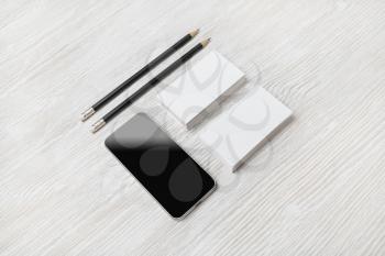 Smartphone, blank business cards and pencils on light wooden background. Blank branding mockup.