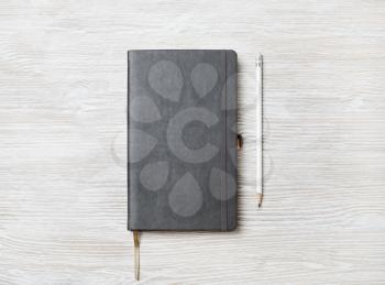 Black notebook and pencil on light wooden background. Space for your text. Flat lay.