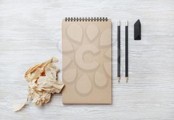 Photo of blank kraft sketchbook, pencil, eraser and crumpled paper on light wooden background. Flat lay.