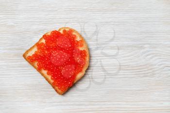 Sandwich with red caviar on light wood table background. Top view. Flat lay.
