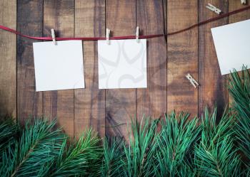 Blank photo paper attach to rope with clothespins and spruce branches on wooden background.
