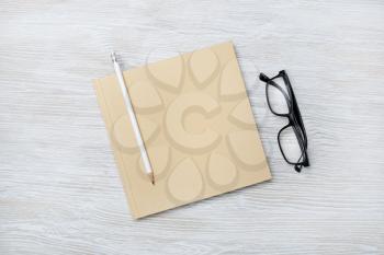 Photo of blank closed sketchbook, pencil and glasses on wooden background. Responsive design mockup. Top view. Flat lay.