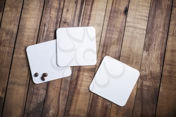 Photo of three blank white square beer coasters and coffee beans on wood table background. Top view. Flat lay.