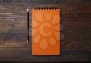 Blank orange notebook and pencil on wooden background. Stationery mock up. Flat lay.