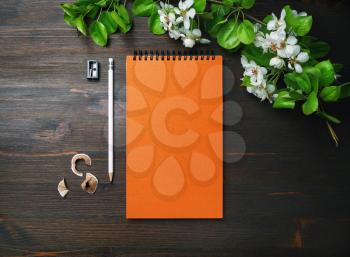 Branding mock up. Orange notebook, pencil, sharpener and spring flowers on wood table background. Flat lay.