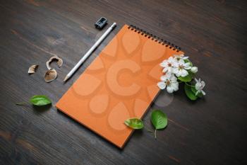 Blank stationery set on wooden background. Orange notebook, pencil, sharpener and flowers.