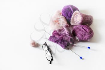 Knitting threads, knitting needles and glasses on white table background.