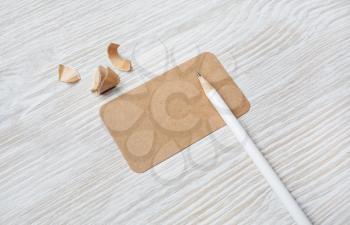 Blank kraft business card and pencil on light wooden background. Mock-up for branding identity.