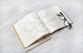 Photo of open book with blank pages, glasses and pencil on light wood table background. Responsive design template.