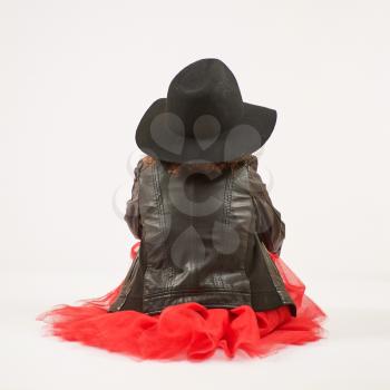Little girl with black hat sitting and pouting. Back view