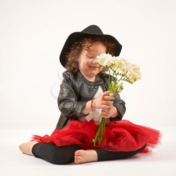 Little girl with black hat sitting and admiring flowers