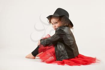 Little girl with black hat sitting and pouting. side view