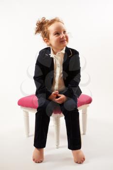 Little girl in black suit sitting on a rose stool and pouting