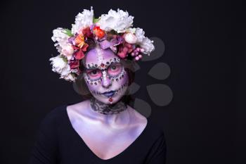 Creative Fashion makeup of a beautiful Halloween model with creative make up,  rhinestones and wreath of flowers on black background
