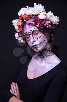 Artistic portrait of a beautiful Halloween model with creative make up,  rhinestones and wreath of flowers on black background
