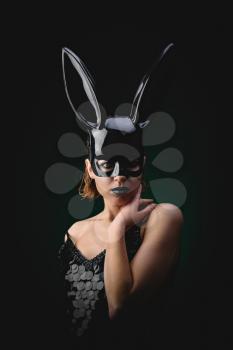 Sexy woman with a Easter bunny black mask standing on a dark background and looks sensually