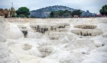 Pamukkale, Turkey – 07.14.2019. Many tourists on Pamukkale white Mountain. Panoramic view from the side of the village on a cloudy summer evening.