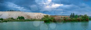 Pamukkale, Turkey – 07.14.2019. White mountain and green lake in Pamukkale. Panoramic view from the side of the village on a cloudy summer evening.