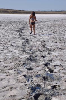 Woman walking along the dry bottom of a salt lake, rear view. Walk the dark-haired woman in a swimsuit on the bottom of a dry lake with salt and mud. The ancient dried-up lake.