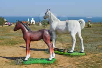 White horse and brown foal. Figures of horses made of plastic on the lawn.