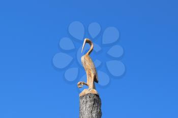 Figure of crane on the stump of a tree against the blue sky. Figures of animals made of wood. Woodcarving.