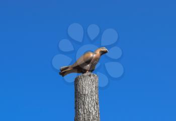 Figurine of a falcon on a stump of a tree against the blue sky. Figures of animals made of wood. Woodcarving.
