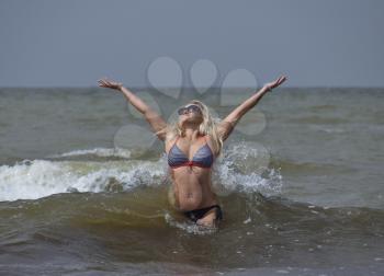 Beautiful blonde standing in sea water. Girl with sunglasses on the sea beach. Rest on the sea beach.
