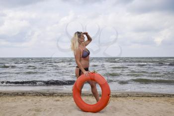 Beautiful blonde with a lifebuoy . Girl sea rescuer. Rest on the sea beach.