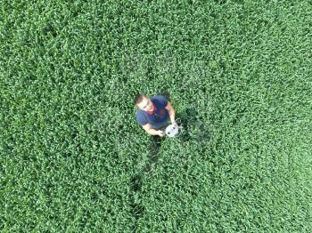 Man holding remote control quadrocopters standing in the green grass on the field.