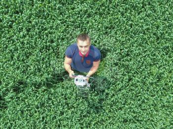 Man holding remote control quadrocopters standing in the green grass on the field.