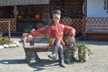 Statue in Cossack fur hat sitting on a bench with a cat. The village leader. Decorative mannequins.
