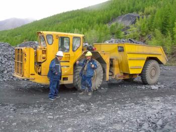 Employees of the gold mining company near the big yellow dump truck with a full body of rubble.          