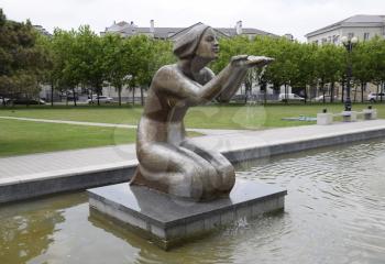 Statue of kneeling woman in the fountain. Water flowing from the hands of the statue.