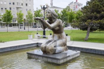Statue of kneeling woman in the fountain. Water flowing from the hands of the statue.