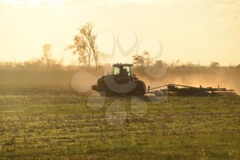 Tractor at sunset plow plow a field. Tilling the soil in the fall after harvest. The end of the season.