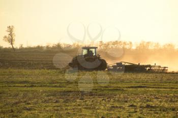 Tractor at sunset plow plow a field. Tilling the soil in the fall after harvest. The end of the season.