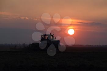 Tractor plowing plow the field on a background sunset. tractor silhouette on sunset background.