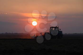 Tractor plowing plow the field on a background sunset. tractor silhouette on sunset background.