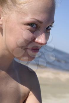 Girl blonde smiling, looking into the camera. Girl on a background of sea water and sandy beach. Beautiful young woman.