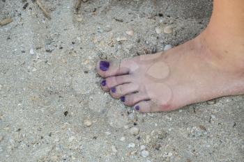 Women's foot with painted purple fingernails. Leg standing on the sand. Pedicure.