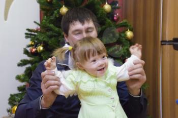 Year-old girl with dad in the background of the Christmas tree. A child with gray eyes and blond hair.