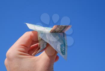 Denominations of Russian money, folded in the airplane against the blue sky in hand.